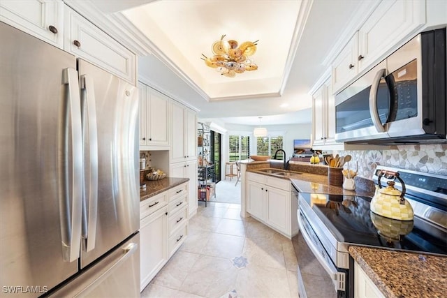 kitchen with appliances with stainless steel finishes, white cabinetry, sink, dark stone countertops, and a raised ceiling