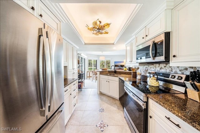 kitchen with appliances with stainless steel finishes, a tray ceiling, sink, white cabinets, and kitchen peninsula