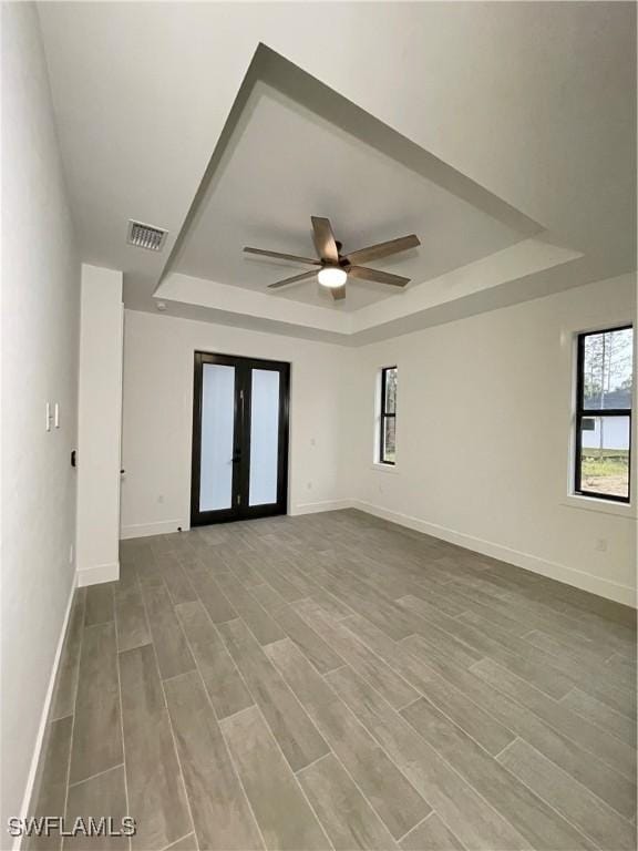 empty room with hardwood / wood-style flooring, a raised ceiling, ceiling fan, and french doors