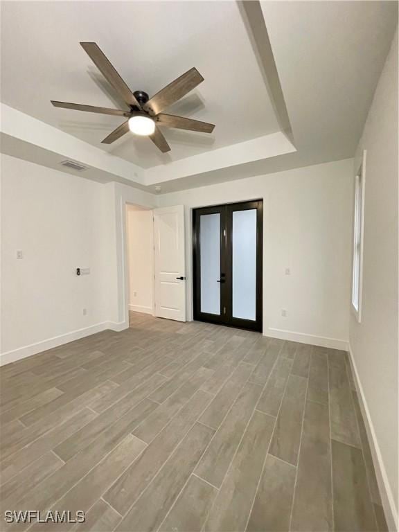 empty room with a tray ceiling, wood-type flooring, french doors, and ceiling fan