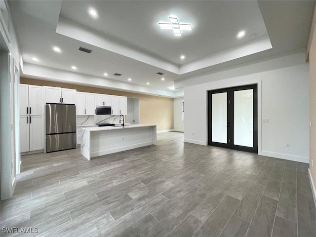 kitchen featuring a kitchen island with sink, stainless steel appliances, white cabinets, french doors, and a raised ceiling