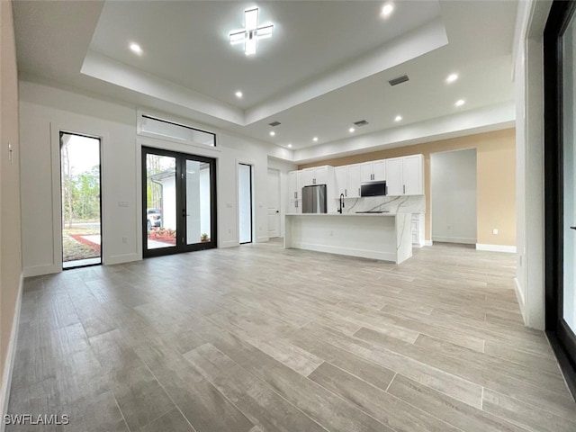 unfurnished living room with french doors, sink, a raised ceiling, and light hardwood / wood-style floors