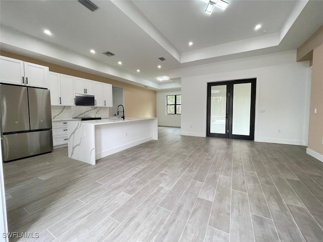 kitchen with white cabinetry, an island with sink, stainless steel fridge, and a tray ceiling