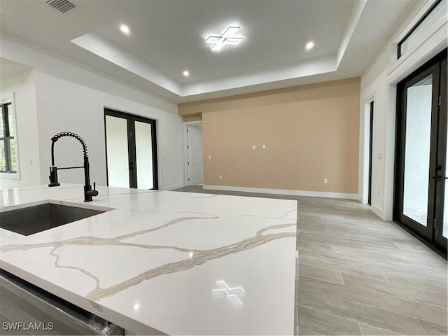 kitchen featuring french doors, a tray ceiling, sink, and light stone counters