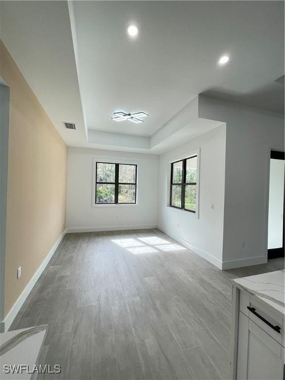 unfurnished living room featuring a raised ceiling and light wood-type flooring