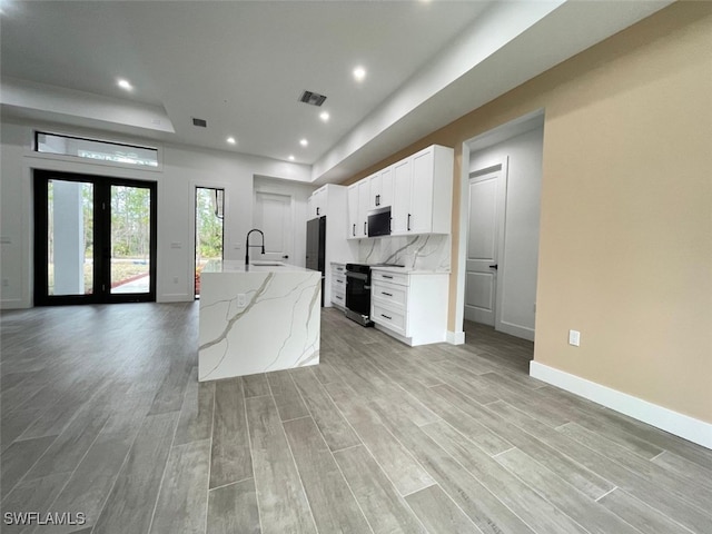 kitchen featuring sink, white cabinetry, backsplash, light stone countertops, and an island with sink