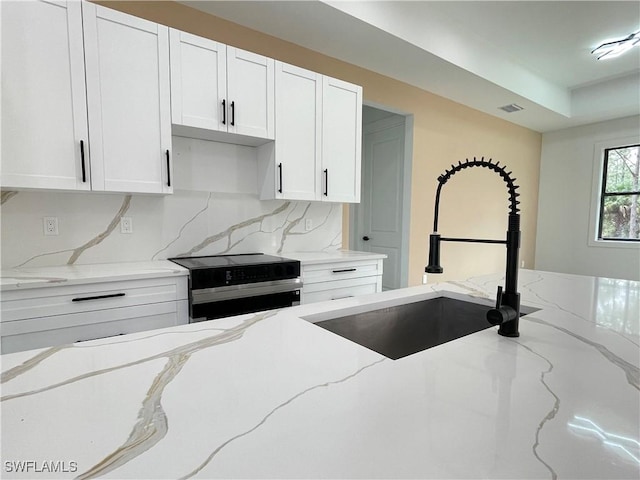 kitchen with light stone counters, stainless steel range with electric stovetop, white cabinetry, and sink