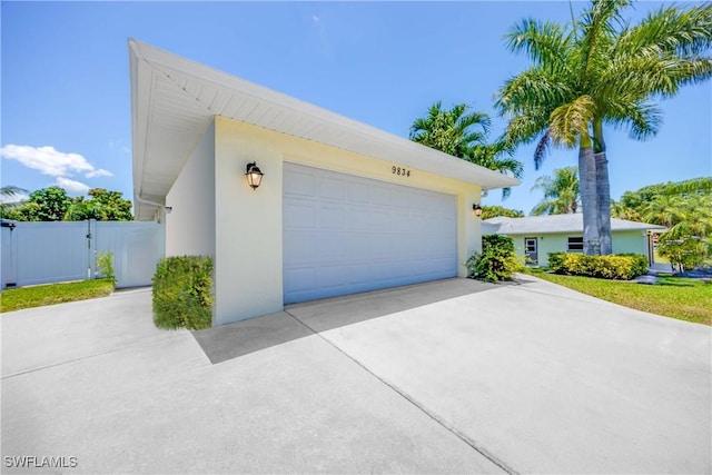 garage featuring concrete driveway, fence, and a gate