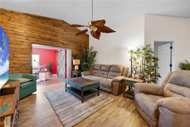 living room featuring light wood-type flooring, wooden walls, high vaulted ceiling, and a ceiling fan