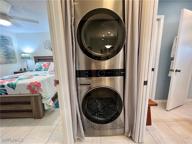 clothes washing area with light tile patterned flooring, stacked washer and dryer, ceiling fan, and a textured ceiling