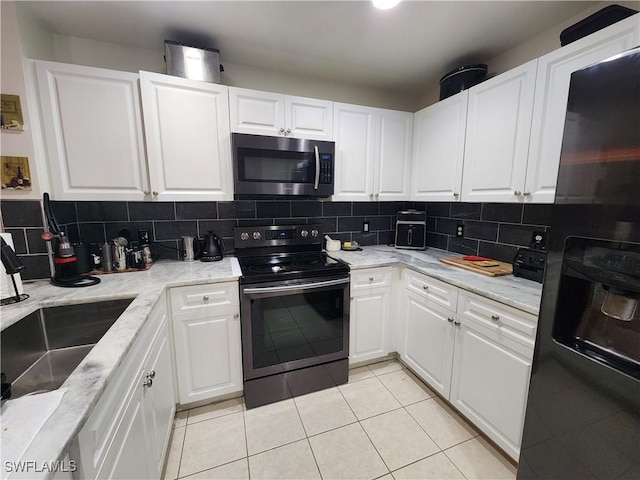 kitchen with appliances with stainless steel finishes, sink, white cabinets, decorative backsplash, and light tile patterned floors