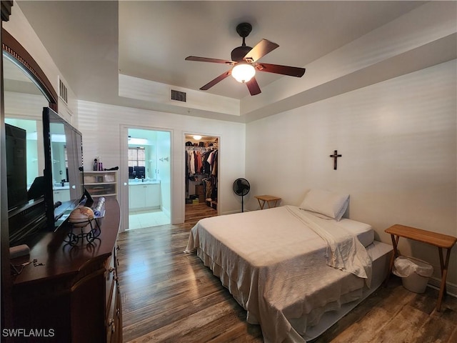 bedroom featuring a walk in closet, a tray ceiling, dark hardwood / wood-style flooring, a closet, and ceiling fan