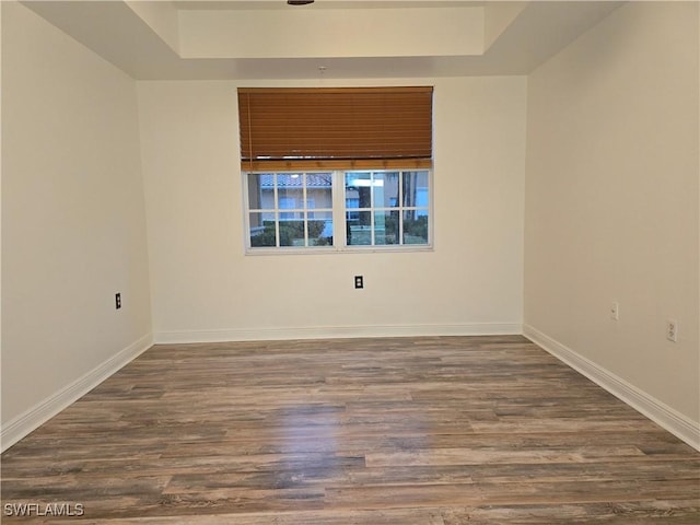 empty room with dark hardwood / wood-style floors and a raised ceiling