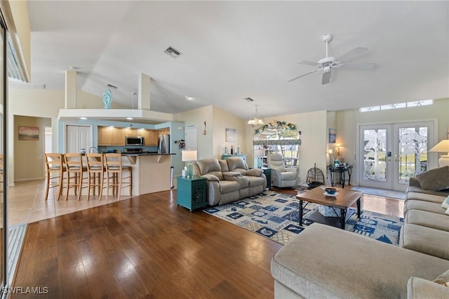 living room with hardwood / wood-style flooring, ceiling fan with notable chandelier, high vaulted ceiling, and french doors