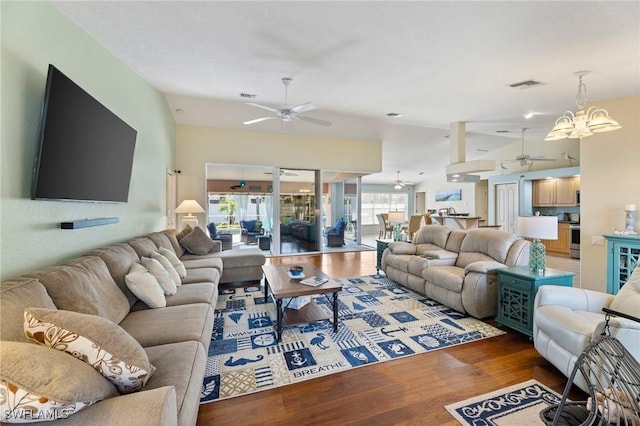 living room featuring lofted ceiling, ceiling fan with notable chandelier, and dark wood-type flooring