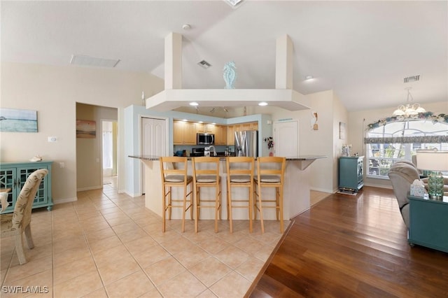 kitchen with lofted ceiling, a chandelier, light wood-type flooring, appliances with stainless steel finishes, and a kitchen breakfast bar