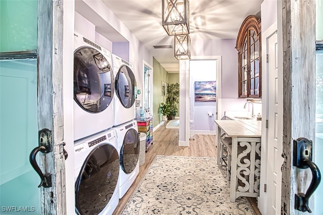 clothes washing area with stacked washer / drying machine, sink, and light hardwood / wood-style floors