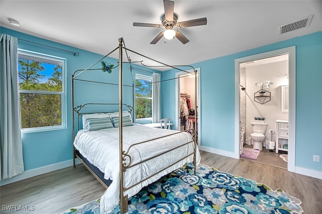 bedroom with multiple windows, ensuite bath, ceiling fan, and hardwood / wood-style flooring