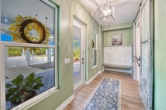 doorway with plenty of natural light, an inviting chandelier, and light wood-type flooring