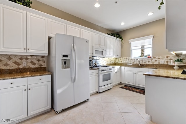 kitchen featuring light tile patterned flooring, white cabinetry, backsplash, dark stone counters, and white appliances