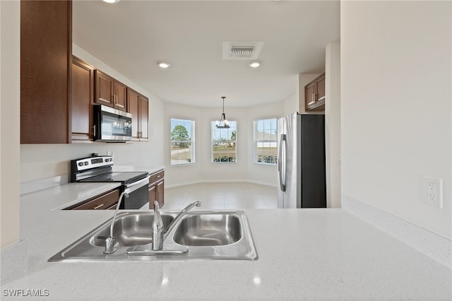 kitchen with sink, appliances with stainless steel finishes, hanging light fixtures, light tile patterned flooring, and kitchen peninsula