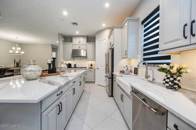 kitchen featuring light stone counters, stainless steel appliances, sink, and hanging light fixtures