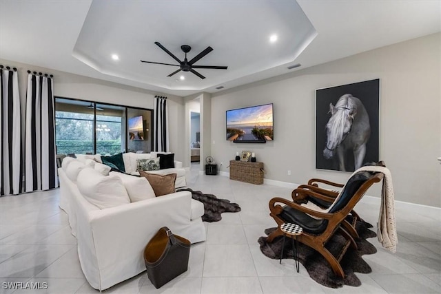 living room with a raised ceiling, light tile patterned floors, and ceiling fan