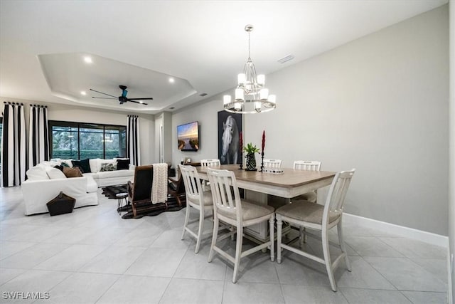 tiled dining area featuring a tray ceiling and ceiling fan with notable chandelier