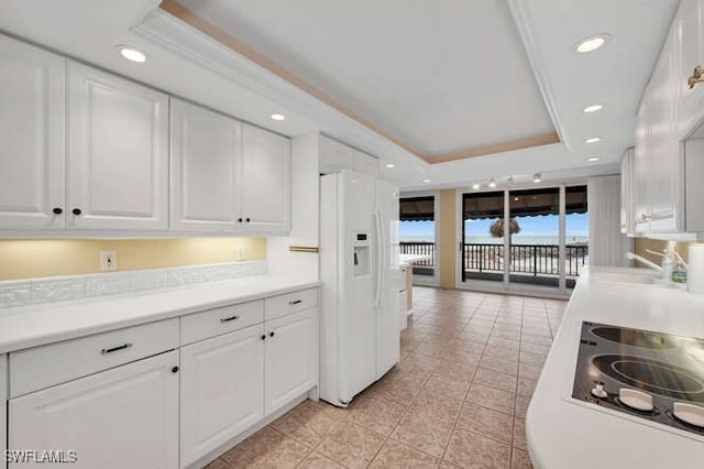 kitchen featuring white fridge with ice dispenser, a tray ceiling, and white cabinets