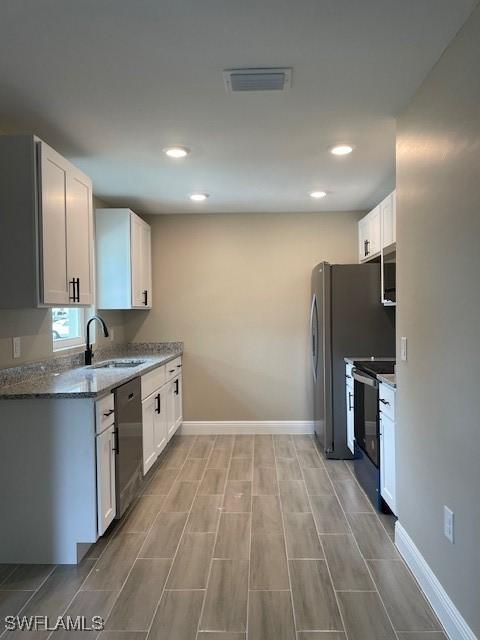 kitchen with stainless steel appliances, white cabinetry, sink, and stone countertops