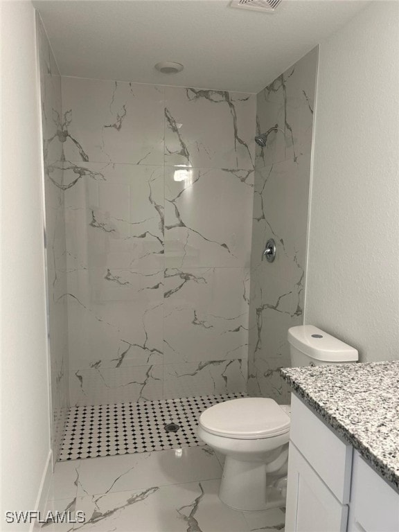 bathroom featuring vanity, a tile shower, and toilet