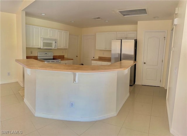 kitchen featuring a spacious island, white appliances, light tile patterned floors, and white cabinets