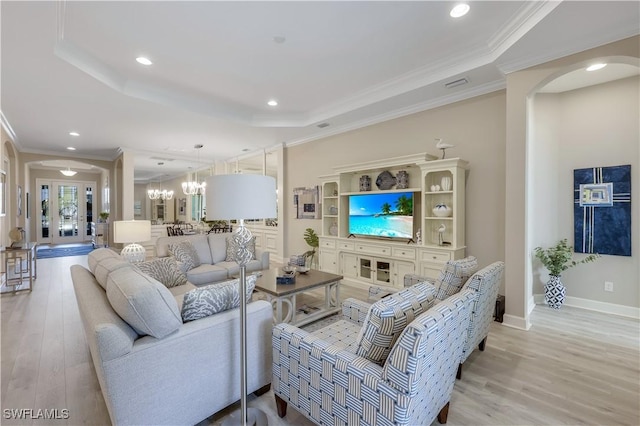 living room featuring a raised ceiling, crown molding, an inviting chandelier, and light hardwood / wood-style flooring