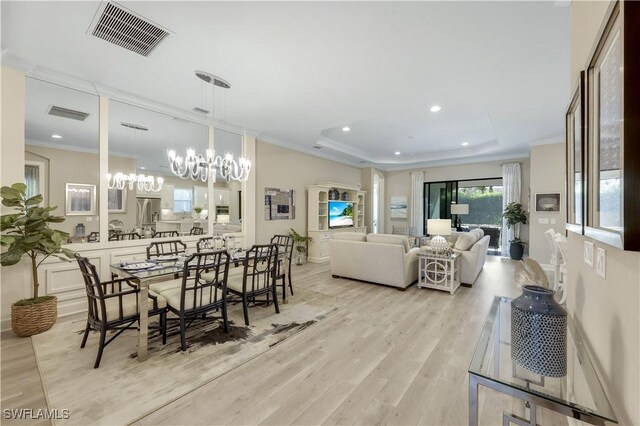 dining room featuring an inviting chandelier, crown molding, light hardwood / wood-style flooring, and a raised ceiling