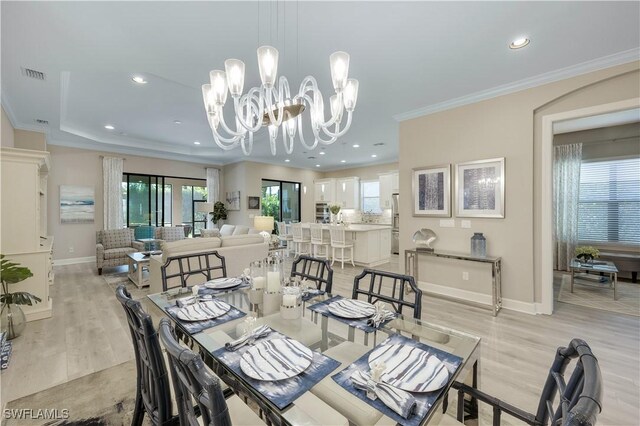 dining space featuring a raised ceiling, crown molding, a chandelier, and light hardwood / wood-style flooring