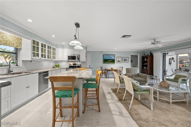 kitchen with sink, white cabinetry, hanging light fixtures, stainless steel appliances, and light stone countertops