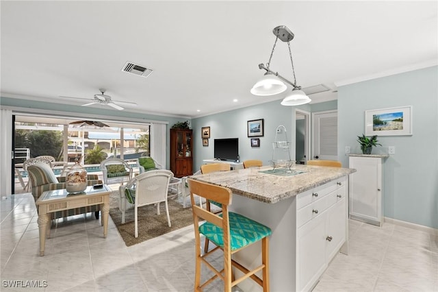 kitchen featuring pendant lighting, ceiling fan, a kitchen island with sink, light stone countertops, and white cabinets