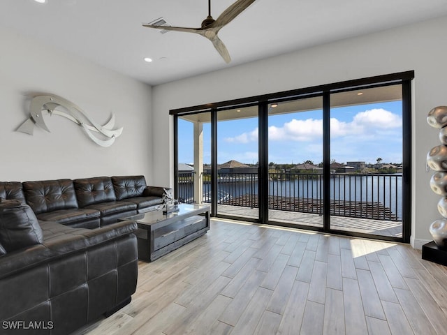 living room featuring ceiling fan, a water view, and light hardwood / wood-style floors