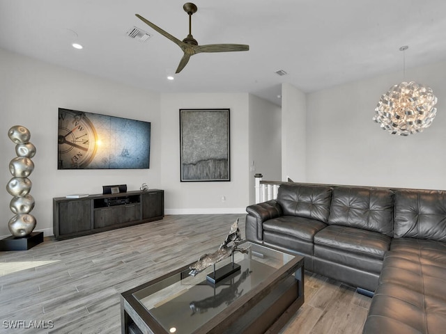 living room featuring ceiling fan with notable chandelier and light wood-type flooring