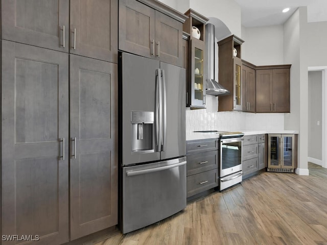 kitchen featuring wall chimney range hood, appliances with stainless steel finishes, wine cooler, tasteful backsplash, and light wood-type flooring