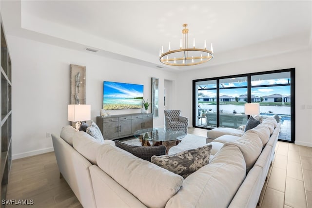 living room with an inviting chandelier, a raised ceiling, and light hardwood / wood-style flooring