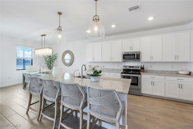 kitchen featuring appliances with stainless steel finishes, a kitchen island with sink, hanging light fixtures, and white cabinets