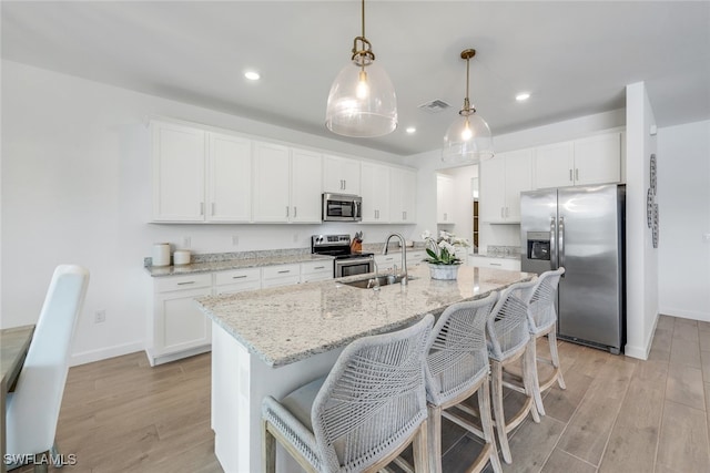 kitchen featuring pendant lighting, sink, appliances with stainless steel finishes, a kitchen island with sink, and white cabinets