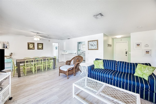 living room with ceiling fan, a textured ceiling, and light wood-type flooring