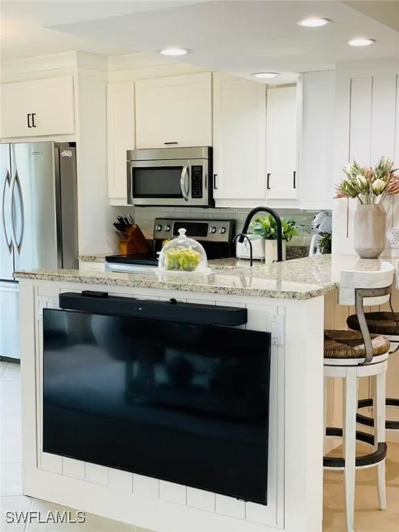 kitchen with appliances with stainless steel finishes, sink, white cabinets, backsplash, and light stone countertops