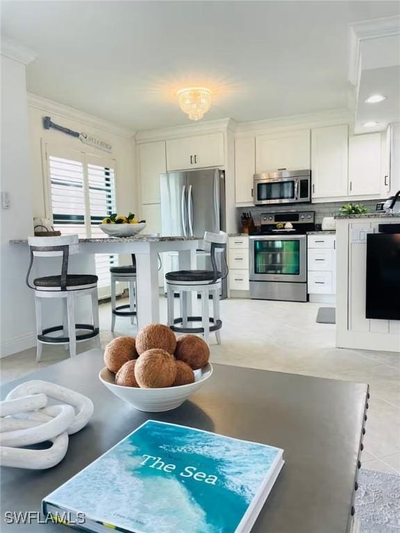 kitchen featuring appliances with stainless steel finishes, a breakfast bar, white cabinetry, backsplash, and ornamental molding