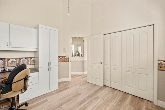 home office with a towering ceiling, light wood finished floors, and baseboards