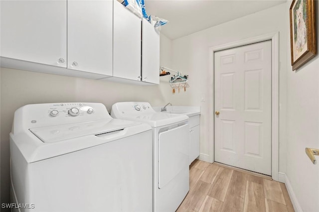 washroom with cabinet space, baseboards, light wood-style floors, separate washer and dryer, and a sink