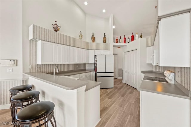 kitchen with white appliances, white cabinetry, a towering ceiling, kitchen peninsula, and light wood-type flooring