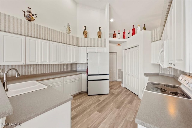 kitchen with white appliances, white cabinets, light wood-style flooring, a high ceiling, and a sink